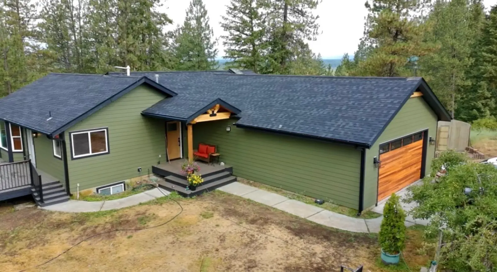 Finished dark shingle roof on a green sided home surrounded by pines