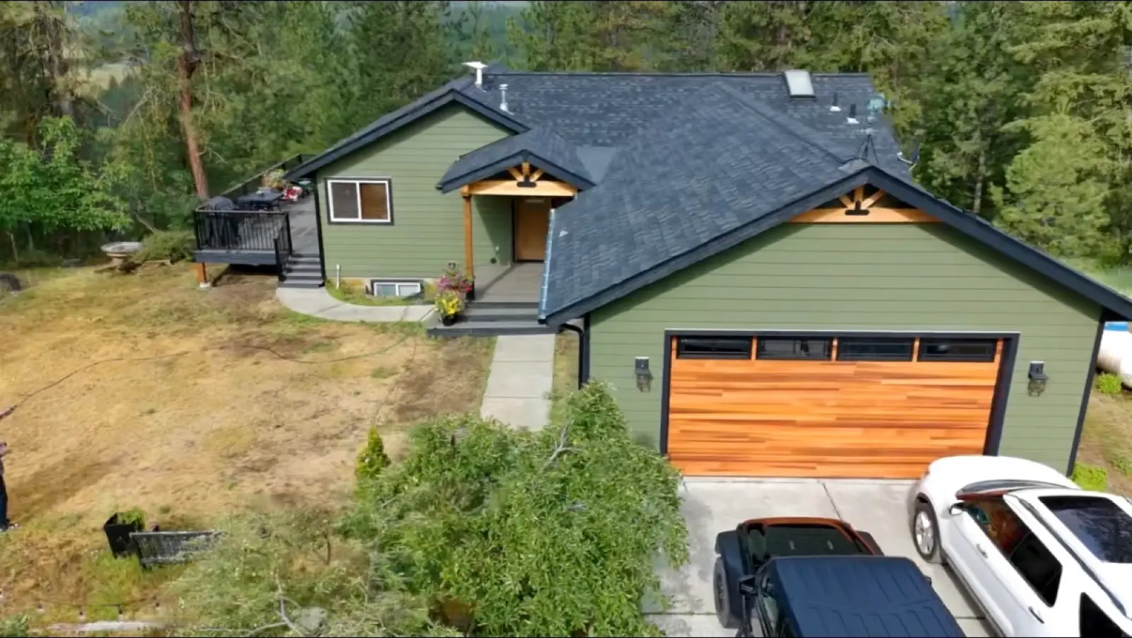 Aerial view of a finished dark shingle roof over a green home with a cedar garage door